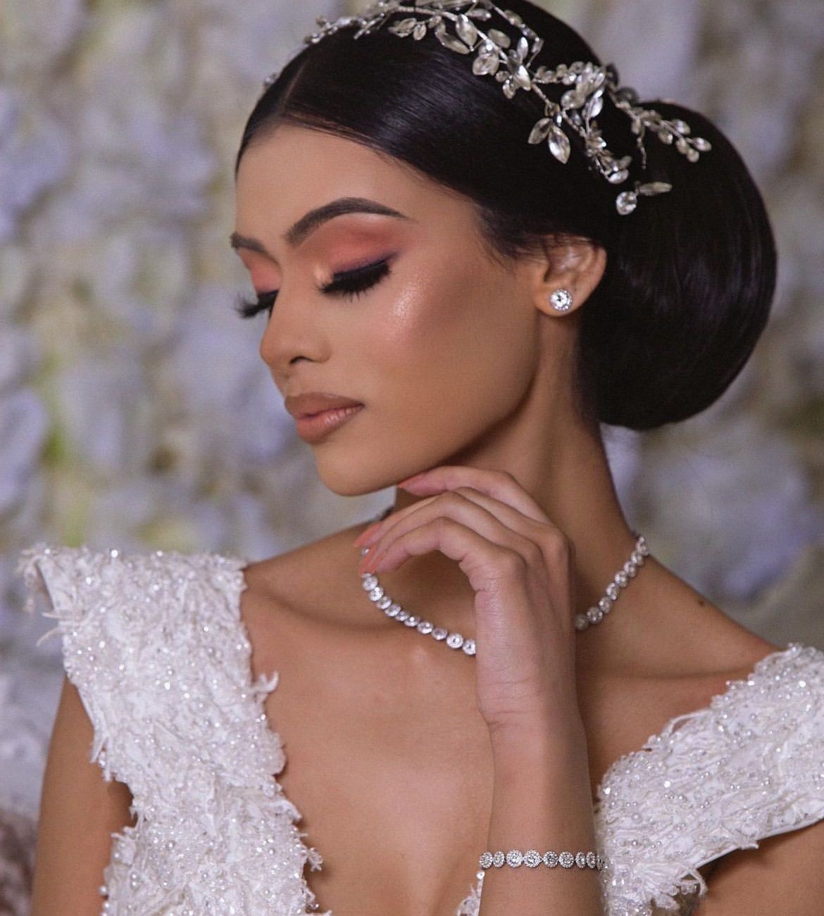 Elegant woman with diamond jewelry and a floral hair accessory, wearing a white gown with intricate details.